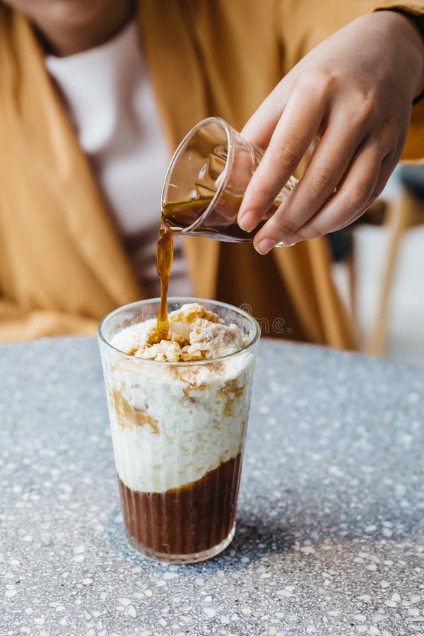 A girl is pouring a shot of espresso in frozen milk mixed with coffee jelly on granite top table. Coffee aroma with fresh milk and chewy coffee jelly. A girl is pouring a shot of espresso in frozen milk mixed with coffee jelly on granite top table. Coffee aroma with fresh milk and chewy coffee jelly.