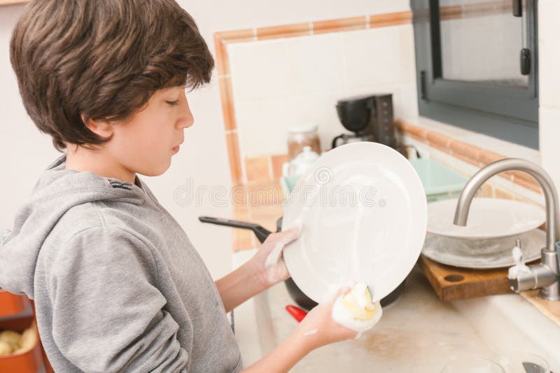 ένα νεαρό αγόρι πλένει ένα βρώμικο πιάτο στην κουζίνα στοκ φωτογραφία με δικαίωμα ελεύθερης χρήσης