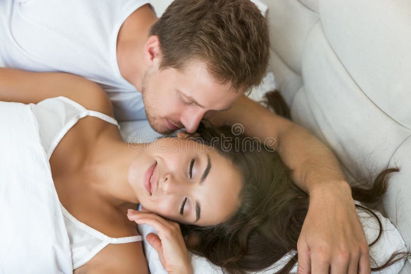 Young couple handsome husband kissing his beautiful sleeping wife in bed in bright bedroomfeeling happy family morning idyll. Young couple handsome husband kissing his beautiful sleeping wife in bed in bright bedroomfeeling happy family morning idyll.