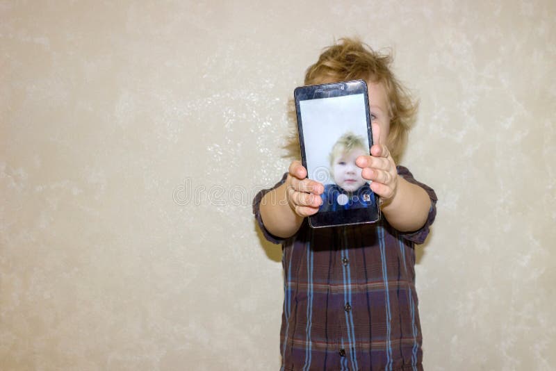 Ένα παιδί αγοριών εξετάζει τη κάμερα ενός smartphone, παρουσιάζει την οθόνη στοκ εικόνα με δικαίωμα ελεύθερης χρήσης Ένα παιδί αγοριών εξετάζει τη κάμερα ενός smartphone, παρουσιάζει την οθόνη στοκ εικόνα με δικαίωμα ελεύθερης χρήσης