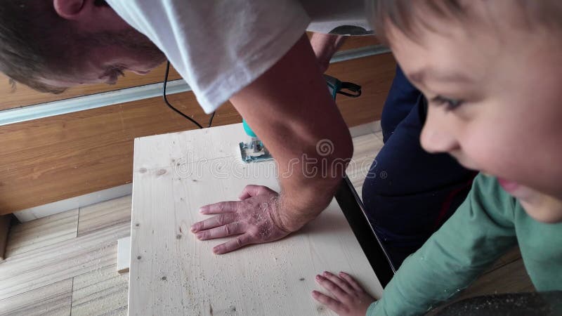Ένα παιδί που βοηθάει τον πατέρα να κρατήσει το ξύλο, ενώ ο μπαμπάς του το κόβει με ένα παζλ. απόθεμα βίντεο
