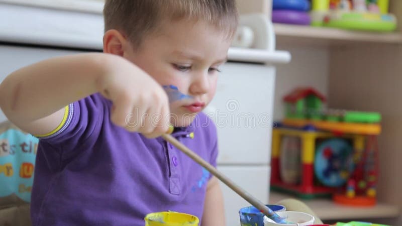 Ένα παιδί σύρει με τα χρωματισμένα χρώματα καθμένος στον πίνακα