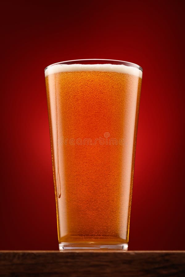 a glass of beer on a wooden stand and a dark red background, pouring beer into a glass, a close view of the object, the beer foams up and bubbles. a glass of beer on a wooden stand and a dark red background, pouring beer into a glass, a close view of the object, the beer foams up and bubbles.