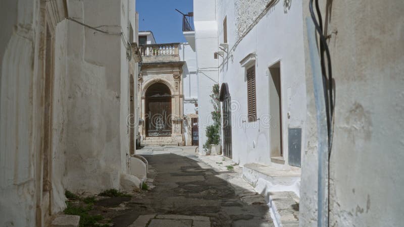 Ένα στενό ηλιόλουστο δρομάκι στην Ιταλία της Μοστουνίας Πούλια παρουσιάζει γοητευτικά ασπρουλιασμένα κτίρια με χαλαστική αρχιτεκτο στοκ φωτογραφία