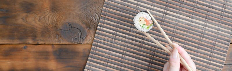 Ένα χέρι με chopsticks κρατά έναν ρόλο σουσιών σε ένα serwing υπόβαθρο χαλιών αχύρου μπαμπού ασιατικά τηγανισμένα τρόφιμα παραδοσ στοκ εικόνα με δικαίωμα ελεύθερης χρήσης Ένα χέρι με chopsticks κρατά έναν ρόλο σουσιών σε ένα serwing υπόβαθρο χαλιών αχύρου μπαμπού ασιατικά τηγανισμένα τρόφιμα παραδοσ στοκ εικόνα με δικαίωμα ελεύθερης χρήσης