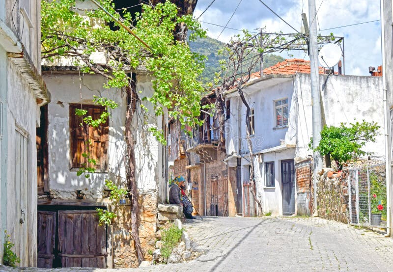Ένα χαρακτηριστικό τουρκικό χωριό με μια γυναικεία συνεδρίαση στο βήμα πορτών στοκ εικόνες Ένα χαρακτηριστικό τουρκικό χωριό με μια γυναικεία συνεδρίαση στο βήμα πορτών στοκ εικόνες