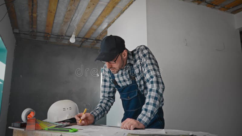 ένας άντρας κάθεται σε ένα τραπέζι ζωγραφισμένος σε χαρτί σε ένα δωμάτιο με ξύλινο δάπεδο απόθεμα βίντεο
