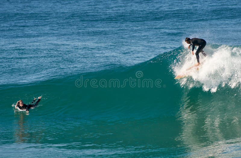 Ένας αρσενικός surfer πιάνει ένα κύμα από μια κοντινή γυναίκα που προσέχει στοκ εικόνες Ένας αρσενικός surfer πιάνει ένα κύμα από μια κοντινή γυναίκα που προσέχει στοκ εικόνες