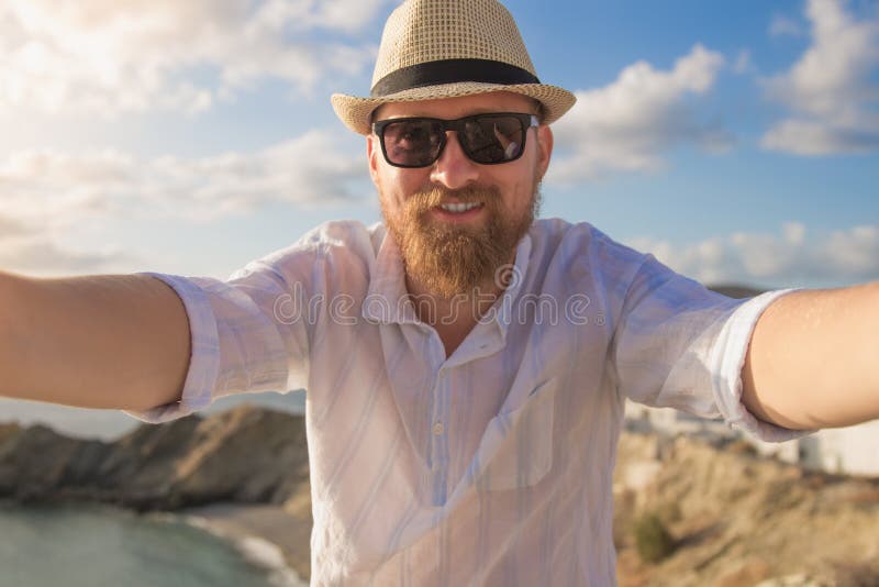 Ένας γενειοφόρος αρσενικός ταξιδιώτης hipster πιπεροριζών κάνει selfie το ηλιόλουστο πρωί με το μπλε νεφελώδες υπόβαθρο άποψης ου στοκ εικόνες Ένας γενειοφόρος αρσενικός ταξιδιώτης hipster πιπεροριζών κάνει selfie το ηλιόλουστο πρωί με το μπλε νεφελώδες υπόβαθρο άποψης ου στοκ εικόνες