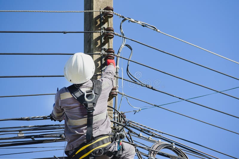 ένας εργαζόμενος σκαρφαλώνει έναν ηλεκτρικό πόλο για να φτιάξει ένα σπασμένο σύρμα φορώντας πλήρη ζώνη ασφαλείας. στοκ φωτογραφία με δικαίωμα ελεύθερης χρήσης