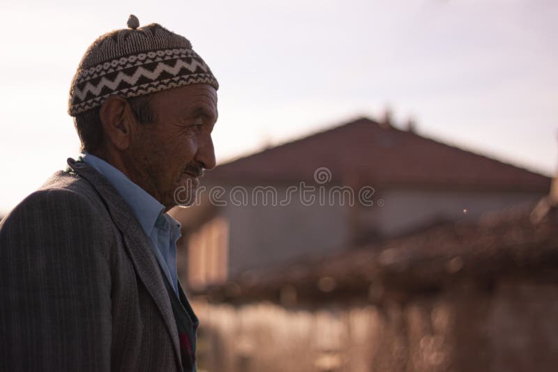 Manisa, Turkey 12/21/2009: Portrait of an elderly Turkish villager wearing a religious hat, jacket, vest and blue shirt. Sun light reflects from his face making wrinkles on the forehead  prominent. Manisa, Turkey 12/21/2009: Portrait of an elderly Turkish villager wearing a religious hat, jacket, vest and blue shirt. Sun light reflects from his face making wrinkles on the forehead  prominent