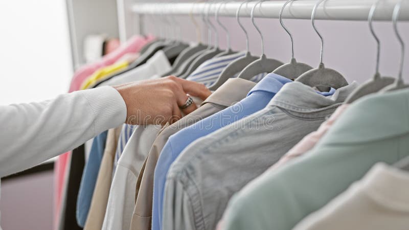 ένας νεαρός άνδρας διαλέγει ένα πουκάμισο από ένα ράφι με διάφορα ρούχα σε ένα φωτεινό δωμάτιο γκαρνταρόμπα στοκ εικόνες