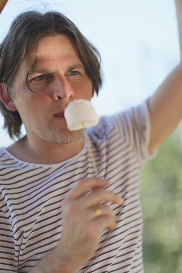 Ένας νεαρός άνδρας κρατά ένα ξύλινο ραβδί με marshmallows στοκ φωτογραφία με δικαίωμα ελεύθερης χρήσης