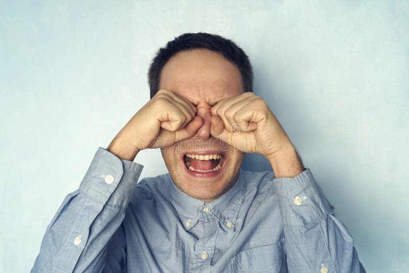 A man cries like a child. A young guy in a shirt with a negative emotion on a blue background. A man cries like a child. A young guy in a shirt with a negative emotion on a blue background