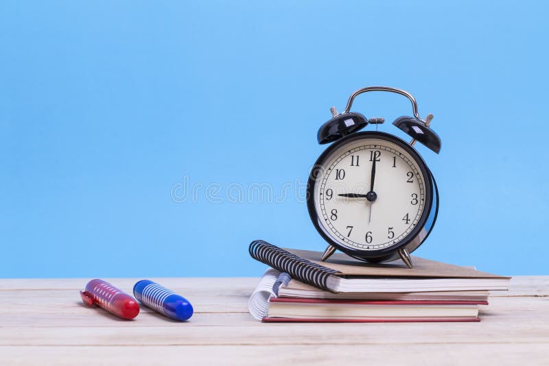 Ένας σωρός των βιβλίων και με τη χρωματισμένα μάνδρα και το ξυπνητήρι σε ένα woode στοκ εικόνες Ένας σωρός των βιβλίων και με τη χρωματισμένα μάνδρα και το ξυπνητήρι σε ένα woode στοκ εικόνες