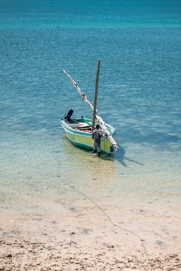 Island of Mozambique / Mozambique - July 8th 2019: A fisherman at a small fishing boat moored in the shallow water at the beach. Nampula Province, Africa. Island of Mozambique / Mozambique - July 8th 2019: A fisherman at a small fishing boat moored in the shallow water at the beach. Nampula Province, Africa