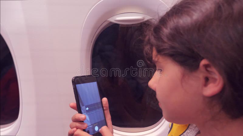 Έννοια αεροσκαφών αεροπορίας το νέο κορίτσι πετά σε ένα εσωτερικό αεροπλάνων παίρνει τις εικόνες στην πόλη νύχτας smartphone κατω
