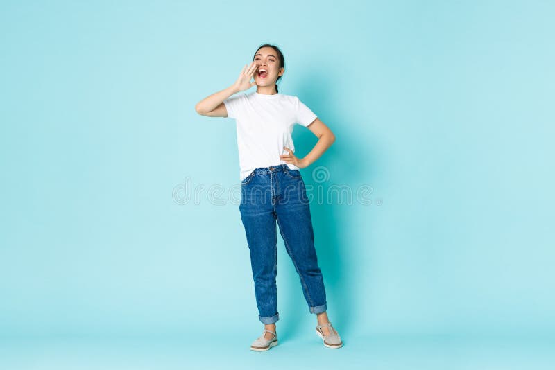 Fashion, beauty and lifestyle concept. Upbeat smiling, attractive asian girl calling for someone, making announcement, shouting loud as if searching person, standing over light blue background. Fashion, beauty and lifestyle concept. Upbeat smiling, attractive asian girl calling for someone, making announcement, shouting loud as if searching person, standing over light blue background.