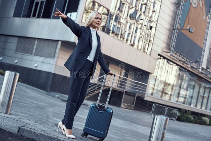 Travel and business trip concept. Smiling young woman with travel bag catching taxi at airport terminal or railway station. Travel and business trip concept. Smiling young woman with travel bag catching taxi at airport terminal or railway station