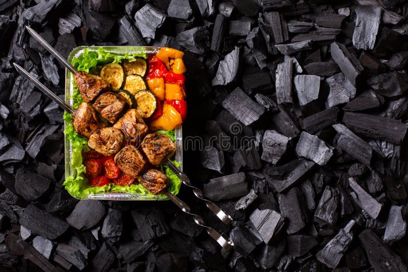 έτοιμο shish kebab. τμήμα κρέατος και λαχανικών που έχουν υποστεί ψήσιμο σε περιέκτη μιας χρήσης στο φόντο του άνθρακα. χώρος αντι