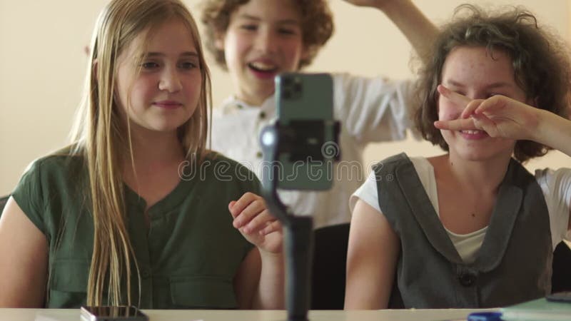 έφηβοι γελάνε και χορεύουν μπροστά από την κάμερα ενός smartphone που βρίσκεται σε τρίποδο. μαθητές κινηματογραφούν τάσεις βίντεο