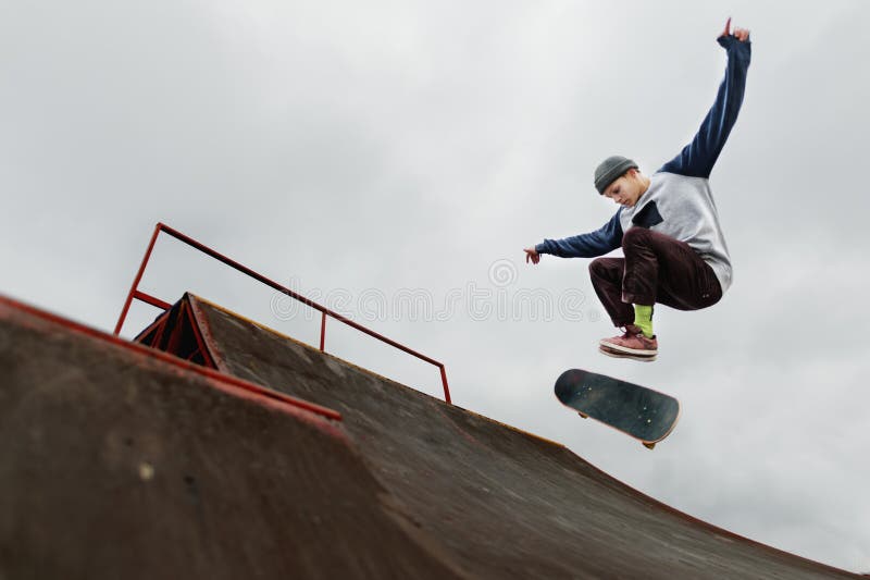 Έφηβος skateboarder σε μια ΚΑΠ που κάνει ένα άλμα τεχνάσματος σε έναν μισό σωλήνα σε ένα νεφελώδες υπόβαθρο ουρανού στοκ φωτογραφίες με δικαίωμα ελεύθερης χρήσης Έφηβος skateboarder σε μια ΚΑΠ που κάνει ένα άλμα τεχνάσματος σε έναν μισό σωλήνα σε ένα νεφελώδες υπόβαθρο ουρανού στοκ φωτογραφίες με δικαίωμα ελεύθερης χρήσης