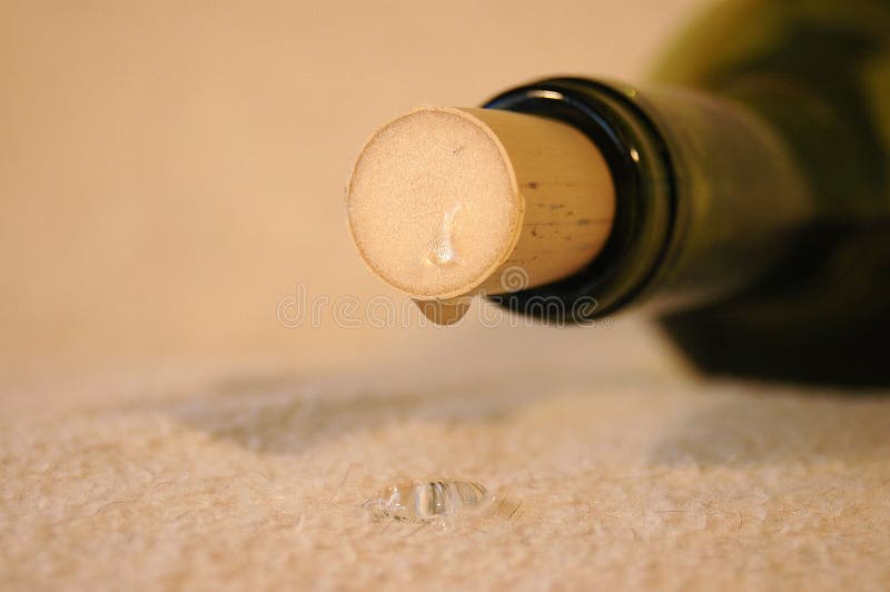 A wine bottle closeup with a damaged cork is leaking and dripping after a party. You can see one drop of alcohol on the floor. What a waste!. A wine bottle closeup with a damaged cork is leaking and dripping after a party. You can see one drop of alcohol on the floor. What a waste!