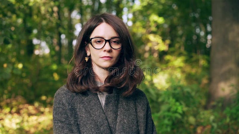 Ήρεμη επιχειρηματίας στην γκρίζα εξέταση τη κάμερα σε ένα πάρκο φθινοπώρου