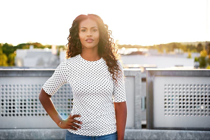 Calm beautiful woman with hand on hip outdoors in front of steel and concrete barrier. Calm beautiful woman with hand on hip outdoors in front of steel and concrete barrier