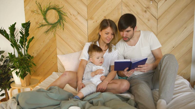 Αγαπώντας οικογένεια τριών που βρίσκονται στο κρεβάτι στο πρωί Οικογένεια που αγκαλιάζει και που διαβάζει το βιβλίο