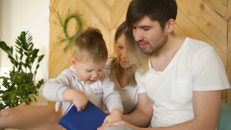 Αγαπώντας οικογένεια τριών που βρίσκονται στο κρεβάτι στο πρωί Οικογένεια που αγκαλιάζει και που διαβάζει το βιβλίο