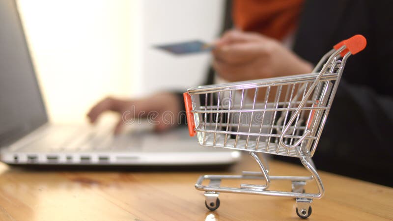 αγορές μέσω διαδικτύου στο internet store κοντεύουν στο καρότσι με ένα καρότσι αγορών με γυναίκα που κάνει αγορά σε φορητό υπολογι στοκ εικόνες