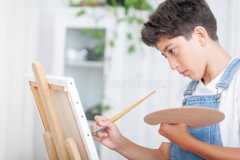 αγόρι στο denim dungarepaint ζωγραφίζοντας με πινέλο και παλέτα χρωμάτων στον καμβά στο σπίτι στοκ εικόνες με δικαίωμα ελεύθερης χρήσης