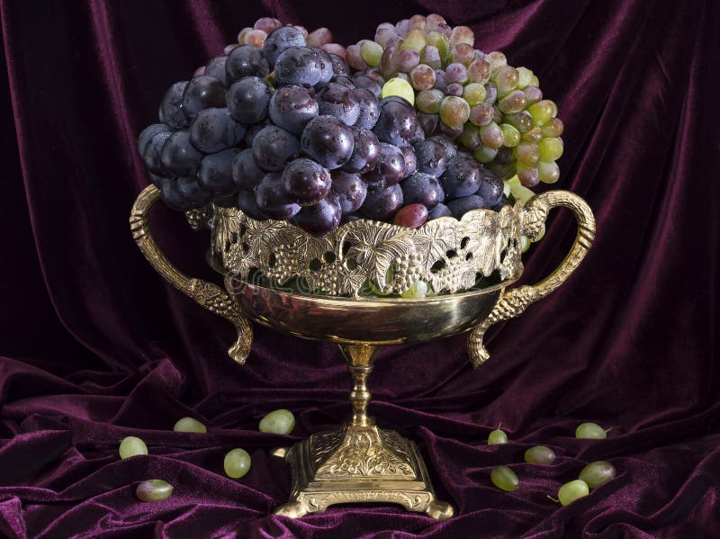 Still life with the decorated vase full of ripe blue and green grape on velvet background. Still life with the decorated vase full of ripe blue and green grape on velvet background