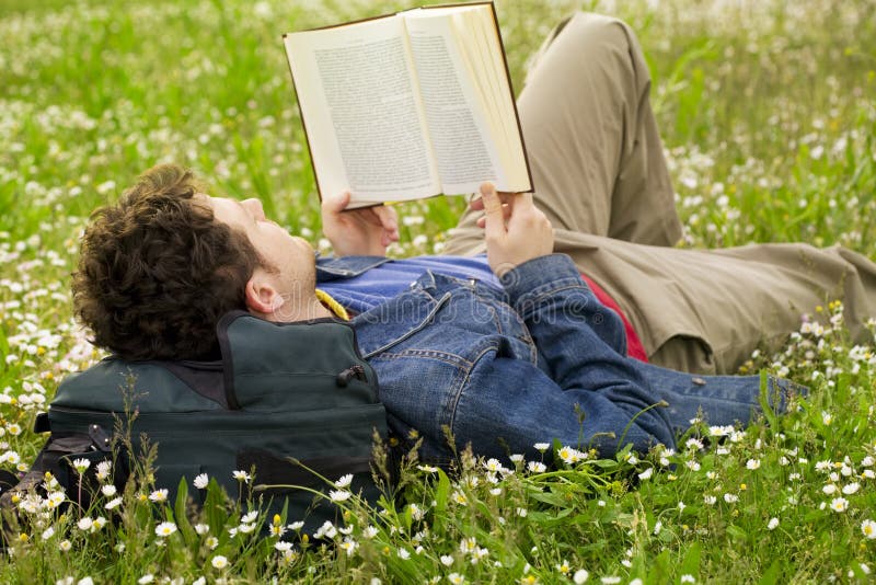 Guy laying on the grass and reading a book. Guy laying on the grass and reading a book