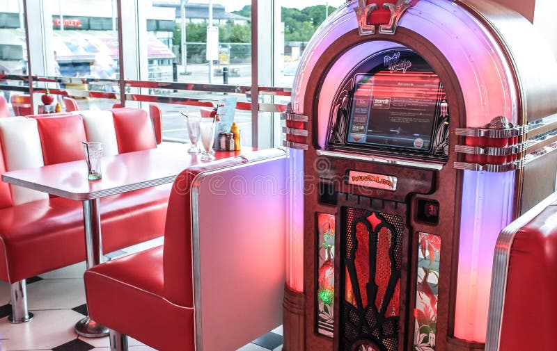 Retro red and white scene of a 1950s style american diner with a vintage wurlitzer jukebox and red and white leather booth seating with steal tables and coca cola glasses and empty mik shake glasses on the table. Neon tubing lighting on the 50s style music system. Retro red and white scene of a 1950s style american diner with a vintage wurlitzer jukebox and red and white leather booth seating with steal tables and coca cola glasses and empty mik shake glasses on the table. Neon tubing lighting on the 50s style music system.