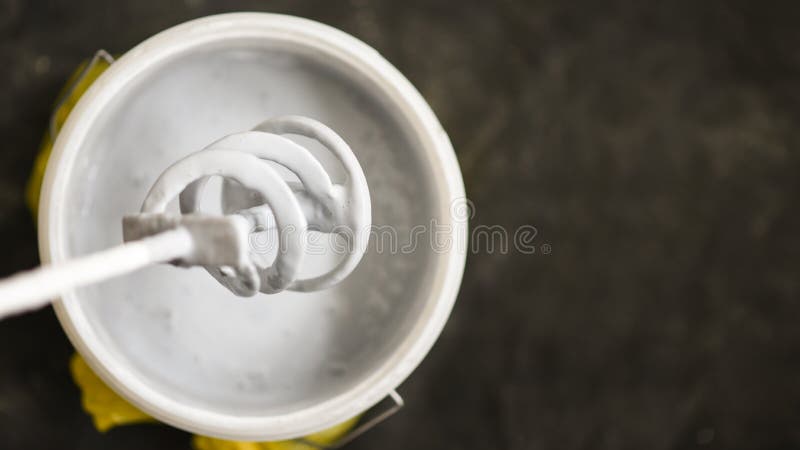 Αναμίκτης κουπιών πέρα από τον κάδο με το άσπρο χρώμα για τον τοίχο, τα εργαλεία DIY και το εξάρτημα, στενός επάνω ροής της δουλε στοκ εικόνες Αναμίκτης κουπιών πέρα από τον κάδο με το άσπρο χρώμα για τον τοίχο, τα εργαλεία DIY και το εξάρτημα, στενός επάνω ροής της δουλε στοκ εικόνες
