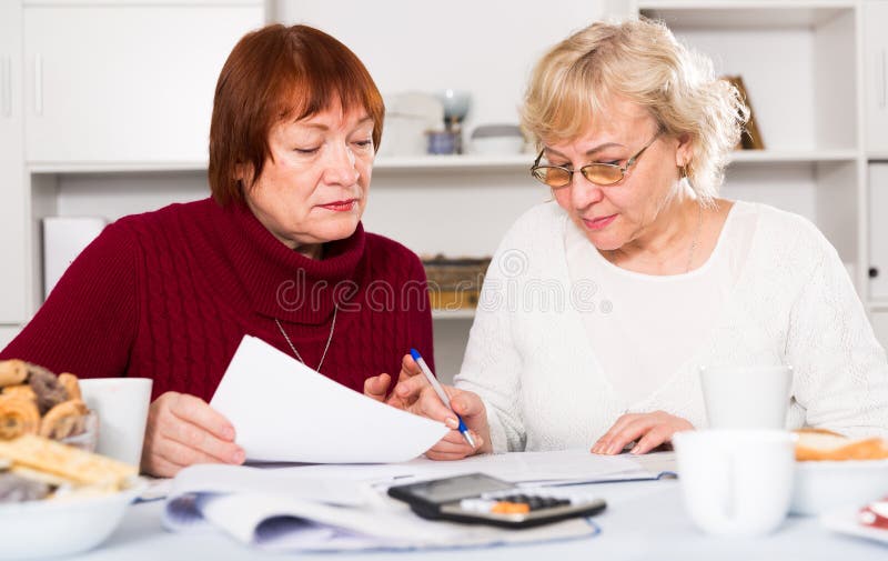 Upset senior ladies attentively reading documents while sitting at home. Upset senior ladies attentively reading documents while sitting at home