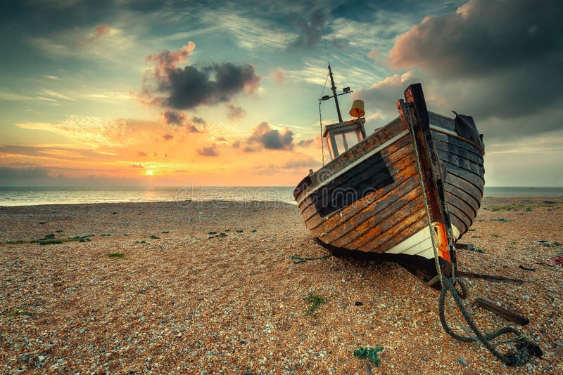 Beautiful sunrise over an old wooden fishing boat on a pebble beach. Beautiful sunrise over an old wooden fishing boat on a pebble beach