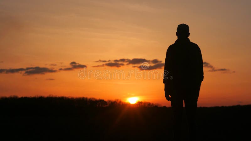 A mans silhouette is seen against the red sky at sunset, standing in front of a beautiful afterglow with trees and clouds in the background. A mans silhouette is seen against the red sky at sunset, standing in front of a beautiful afterglow with trees and clouds in the background