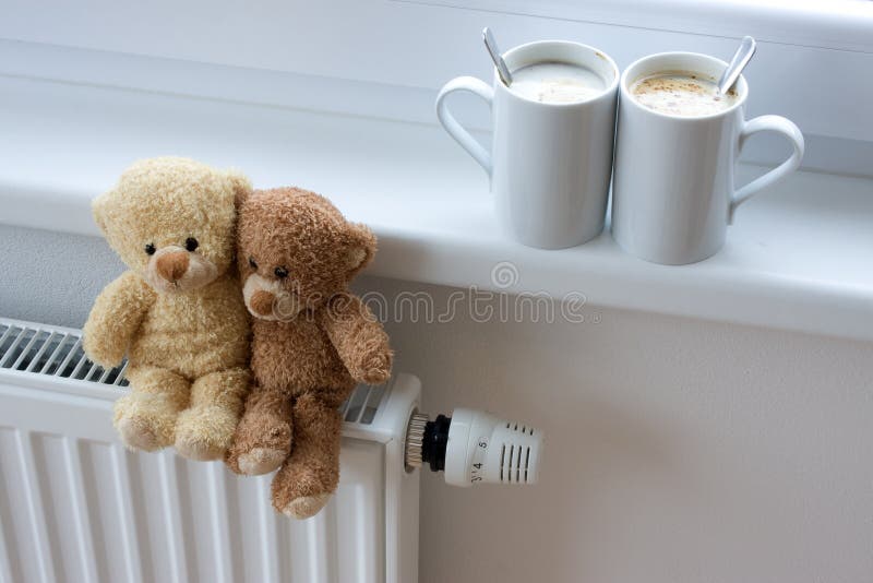Two teddy bears sitting on radiator in home, with coffee cups on windowsill. Two teddy bears sitting on radiator in home, with coffee cups on windowsill