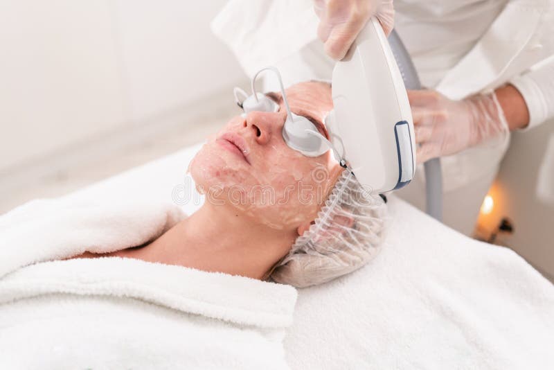 Αντι ακμή phototherapy με τον επαγγελματικό εξοπλισμό Όμορφη γυναίκα στο σαλόνι ομορφιάς κατά τη διάρκεια της διαδικασίας αναζωογ. Αντι ακμή phototherapy με τον επαγγελματικό εξοπλισμό Όμορφες γυναίκες στο σαλόνι ομορφιάς κατά τη διάρκεια της διαδικασίας αναζωογόνησης φωτογραφιών Επεξεργασία δερμάτων προσώπου λέιζερ στην καλλυντική κλινική