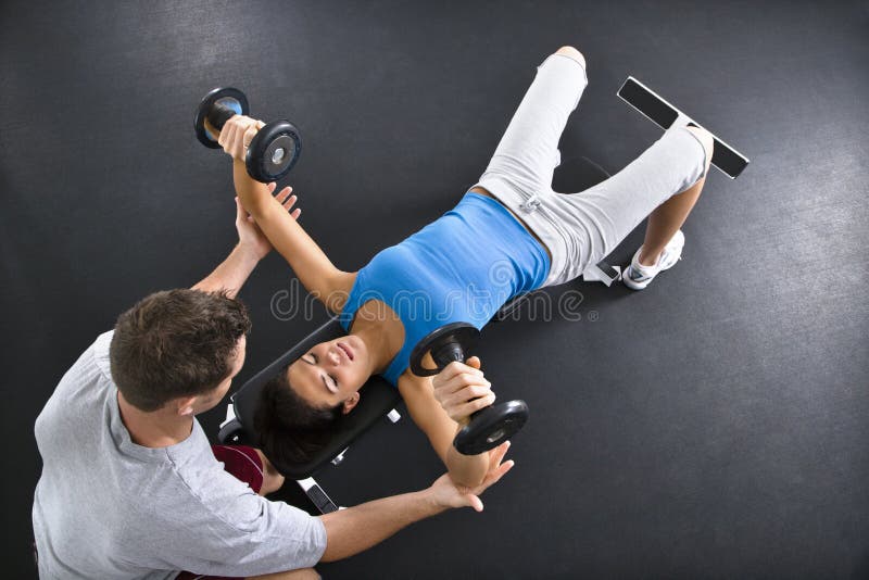 Man assisting woman lifting weights at gym. Man assisting woman lifting weights at gym.