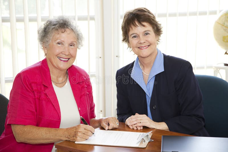 Senior woman signs paperwork in mature businesswoman's office. Senior woman signs paperwork in mature businesswoman's office.