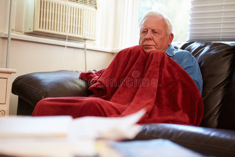 Depressed Senior Man Trying To Keep Warm Under Blanket At Home Looking Worried. Depressed Senior Man Trying To Keep Warm Under Blanket At Home Looking Worried