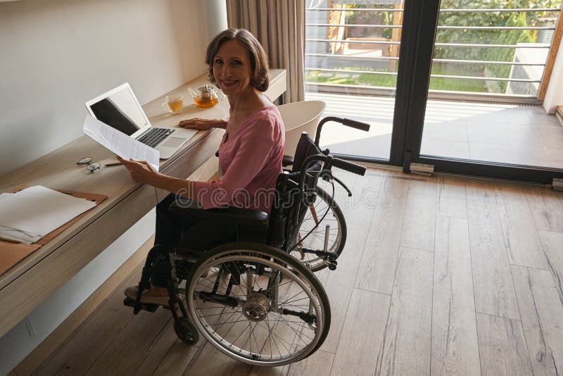 απενεργοποιημένη κυρία που χαμογελά με κάμερα από το γραφείο με φορητό υπολογιστή στοκ εικόνες