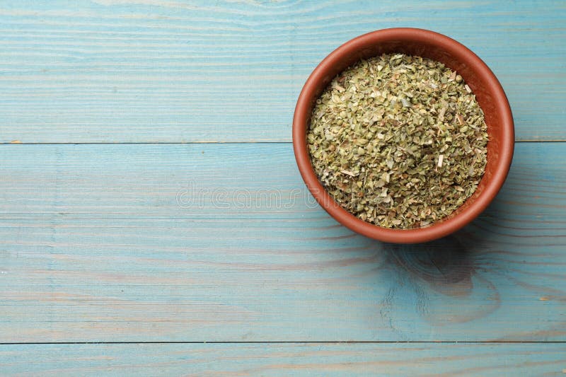 Αποξηραμένο oregano σε μπολ σε ανοιχτό μπλε ξύλινο τραπέζι πάνω όψη. στοκ εικόνες