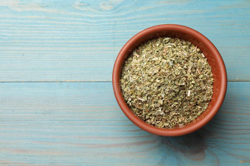 Αποξηραμένο oregano σε μπολ σε ανοιχτό μπλε ξύλινο τραπέζι πάνω όψη. Χώρος κειμένου στοκ εικόνες