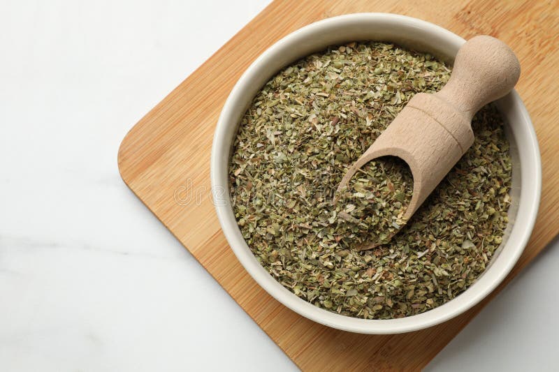 Αποξηραμένο oregano σε μπολ και κουταλιά πάνω σε λευκό μαρμάρινο τραπέζι στοκ φωτογραφία με δικαίωμα ελεύθερης χρήσης