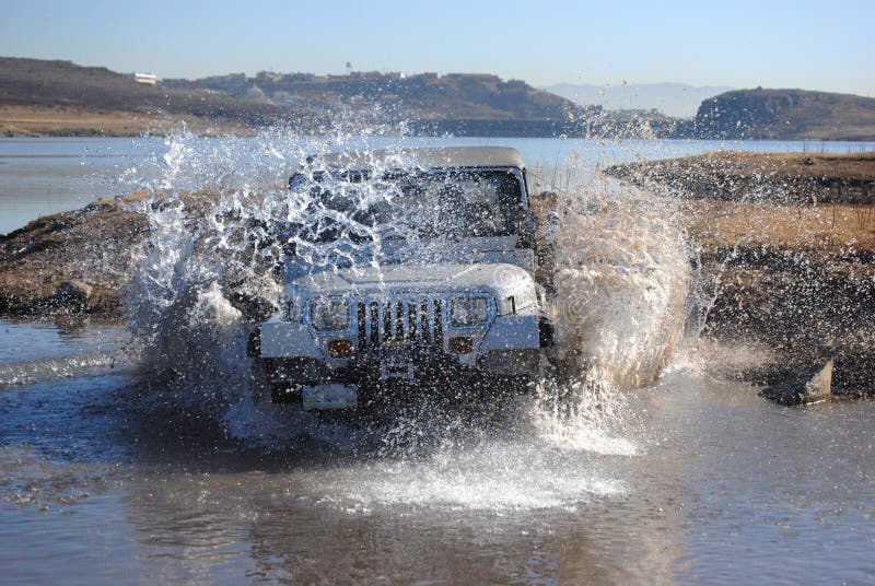 A 4x4 vehicle drives into shallow water creating a big splash. A 4x4 vehicle drives into shallow water creating a big splash.